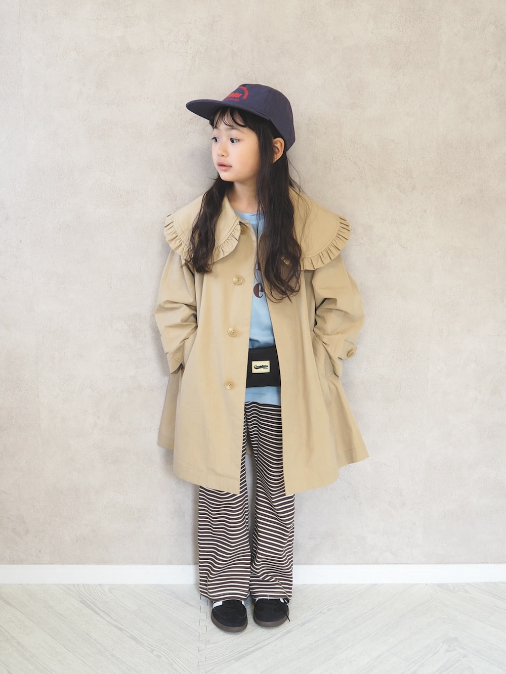 ベージュ系のステンカラーコート、ブラック系のスニーカー、グレー系のTシャツ/カットソーを着用したキッズの春コーディネートの2枚目の写真