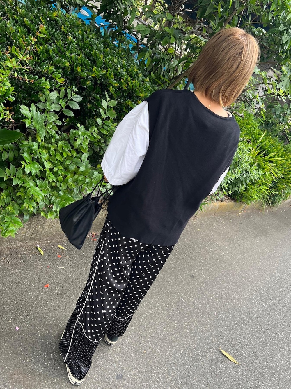 ブラック系のベスト、ブラック系のパンツ、ホワイト系のスニーカーを着用したレディースの夏コーディネートの2枚目の写真