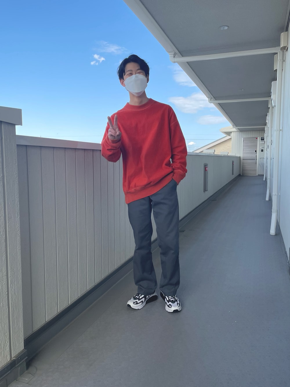 オレンジ系のトップス、グレー系のチノパンツ、ホワイト系のスニーカーを着用したメンズの春コーディネートの3枚目の写真