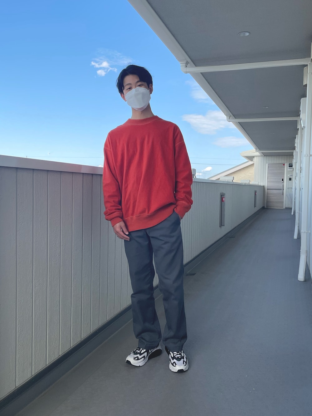 オレンジ系のトップス、グレー系のチノパンツ、ホワイト系のスニーカーを着用したメンズの春コーディネートの2枚目の写真