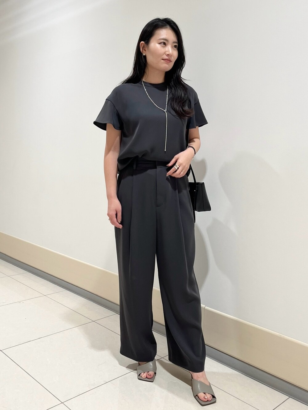 グレー系のシャツ/ブラウス、グレー系のスラックス、ブラック系のショルダーバッグを着用したレディースの春コーディネートの2枚目の写真