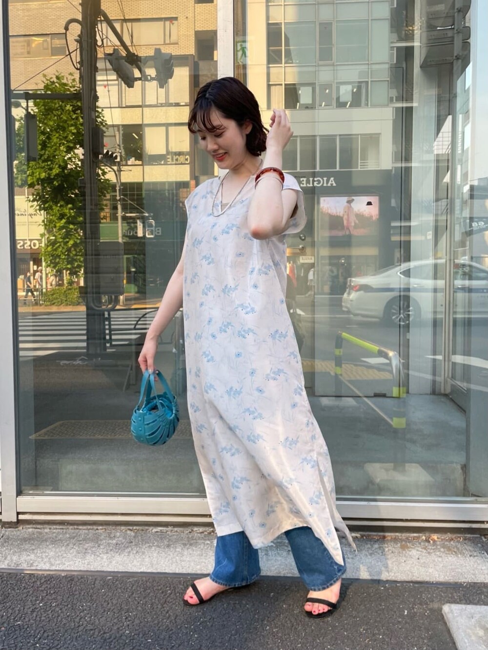 ベージュ系のワンピース、オレンジ系のトートバッグ、ブルー系のデニムパンツを着用したレディースの夏コーディネートの2枚目の写真