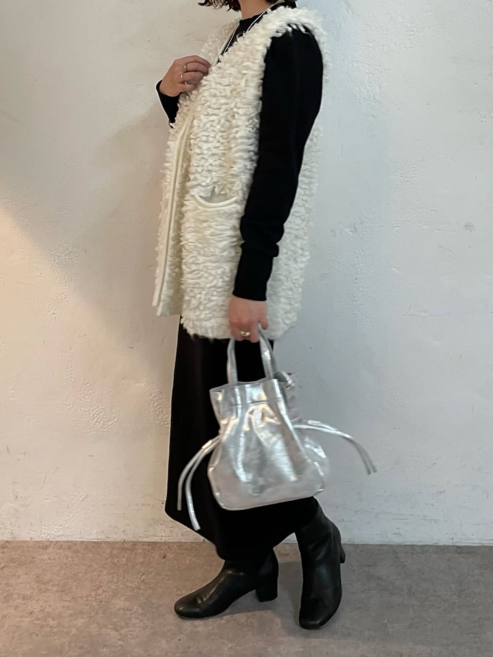 シルバー系のトートバッグ、ブラック系のブーツ、ホワイト系のニット/セーターを着用したレディースの冬コーディネートの2枚目の写真