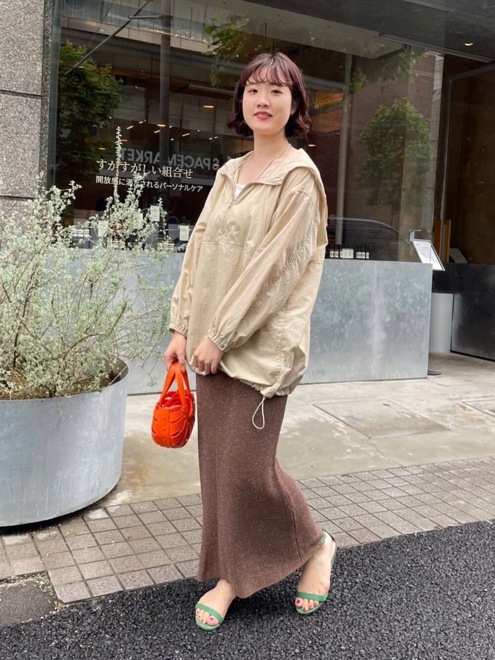 オレンジ系のトートバッグ、ブラウン系のスカート、ベージュ系のブルゾンを着用したレディースの夏コーディネートの2枚目の写真