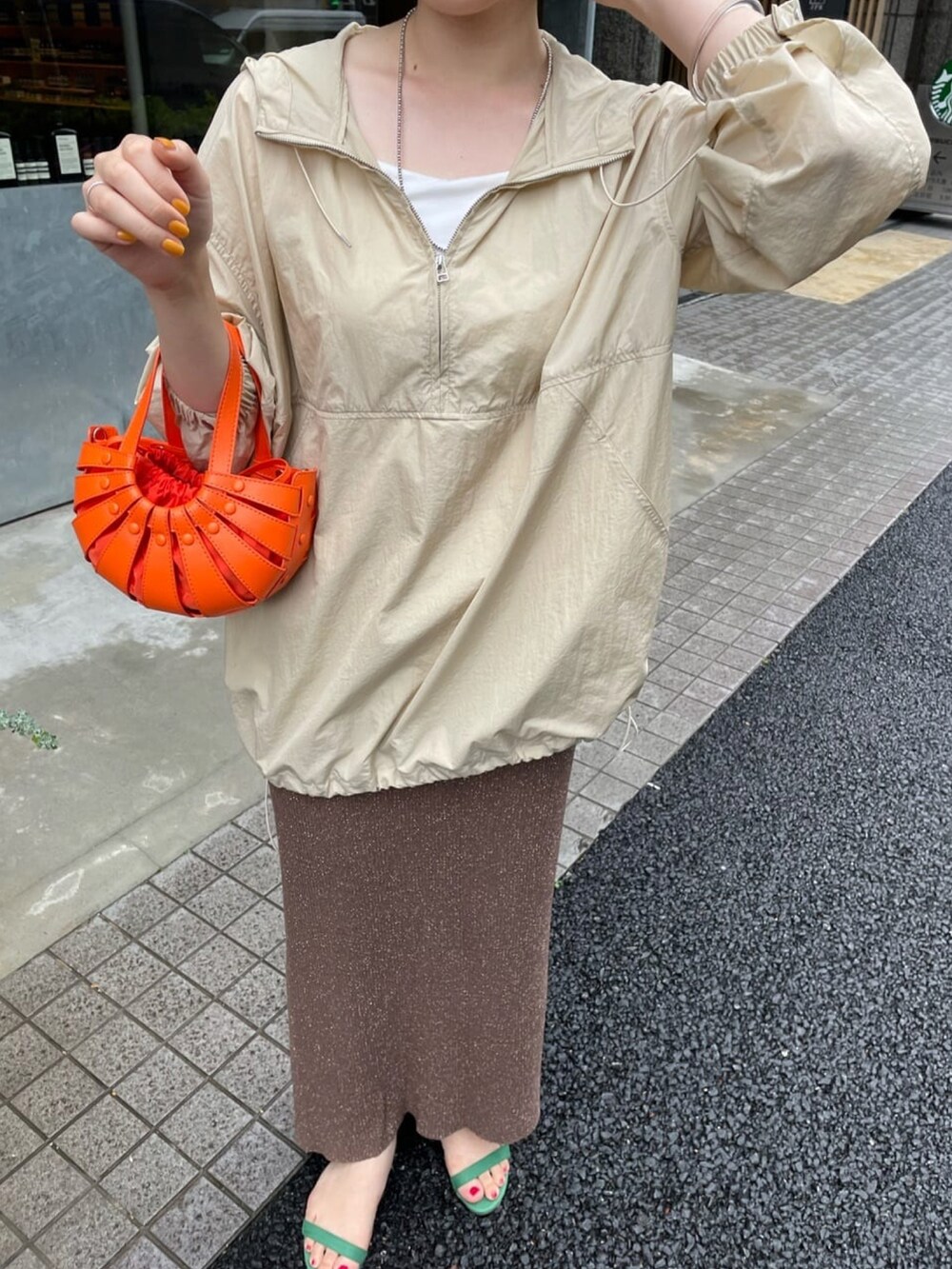 オレンジ系のトートバッグ、ブラウン系のスカート、ベージュ系のブルゾンを着用したレディースの夏コーディネートの4枚目の写真