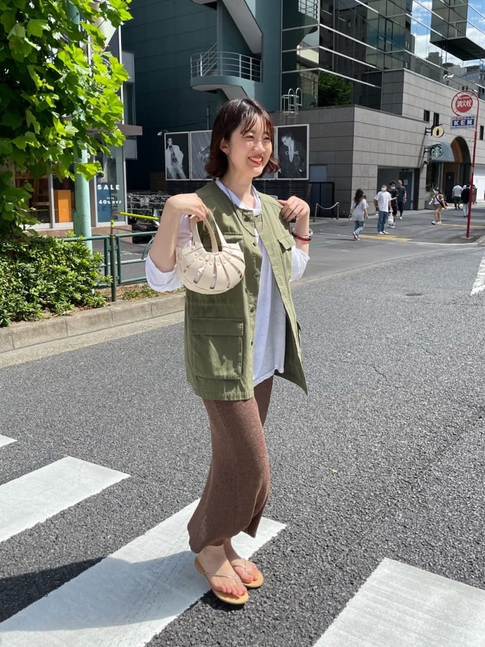 オレンジ系のトートバッグ、グリーン系のベスト、ベージュ系のTシャツ/カットソーを着用したレディースの夏コーディネートの3枚目の写真