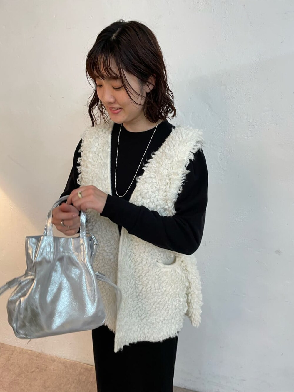 シルバー系のトートバッグ、ブラック系のブーツ、ホワイト系のニット/セーターを着用したレディースの冬コーディネートの5枚目の写真