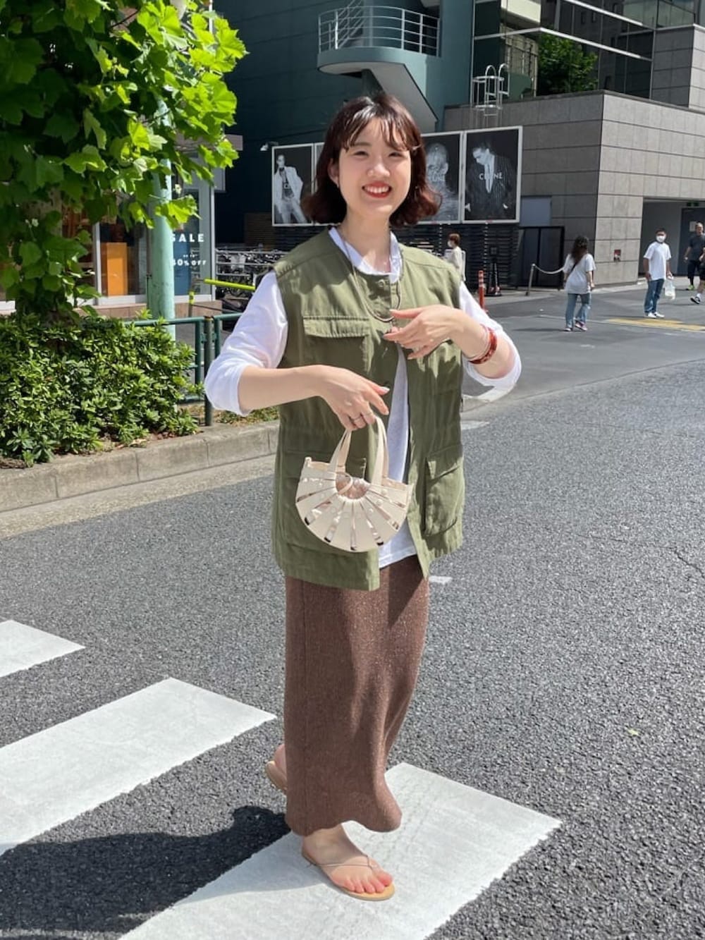 オレンジ系のトートバッグ、グリーン系のベスト、ベージュ系のTシャツ/カットソーを着用したレディースの夏コーディネートの2枚目の写真