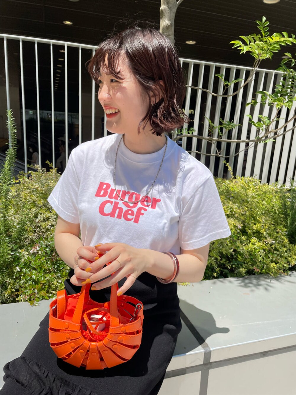 オレンジ系のトートバッグ、ブラック系のスカート、ホワイト系のTシャツ/カットソーを着用したレディースの夏コーディネートの2枚目の写真