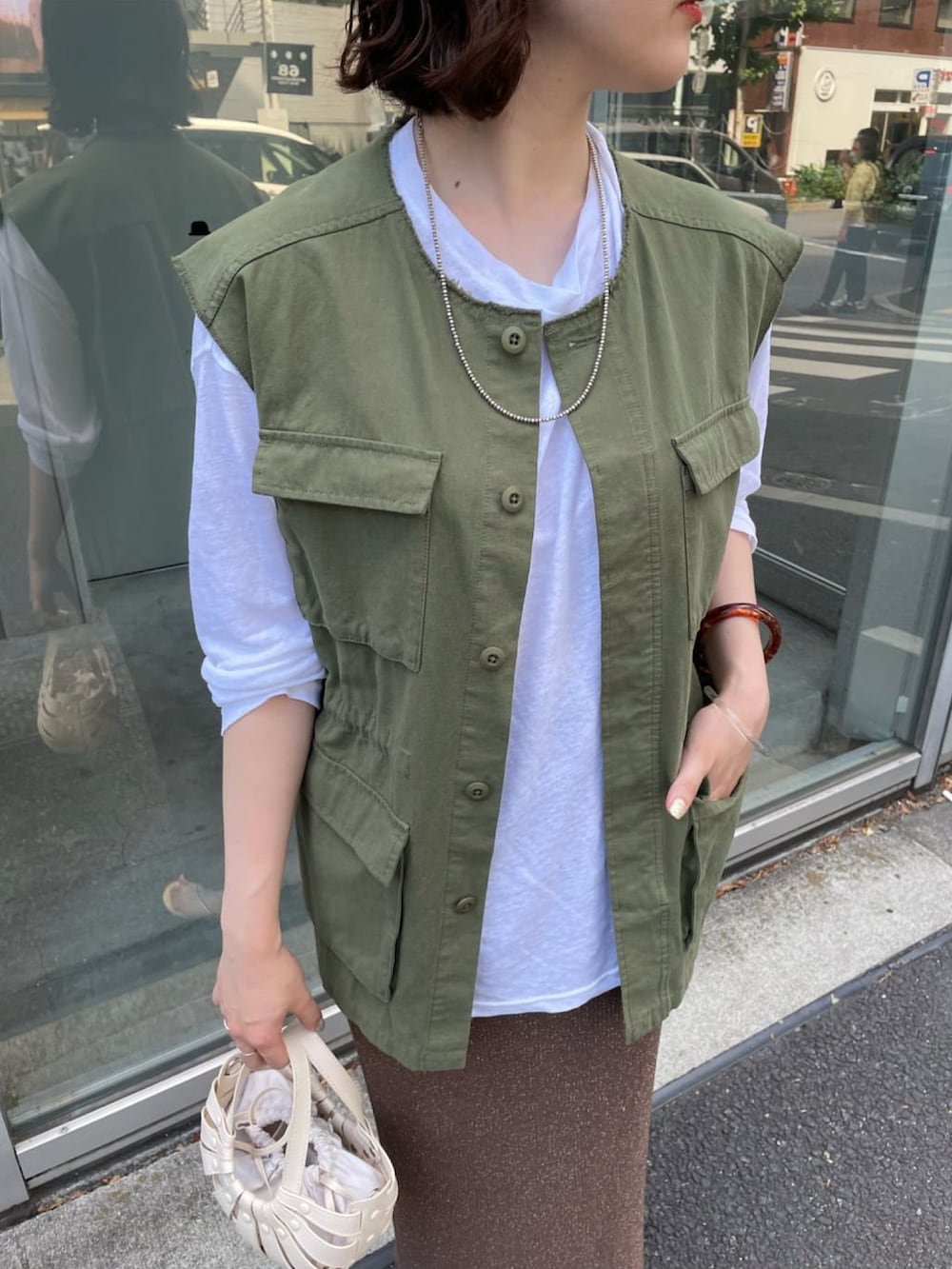 オレンジ系のトートバッグ、グリーン系のベスト、ベージュ系のTシャツ/カットソーを着用したレディースの夏コーディネートの4枚目の写真