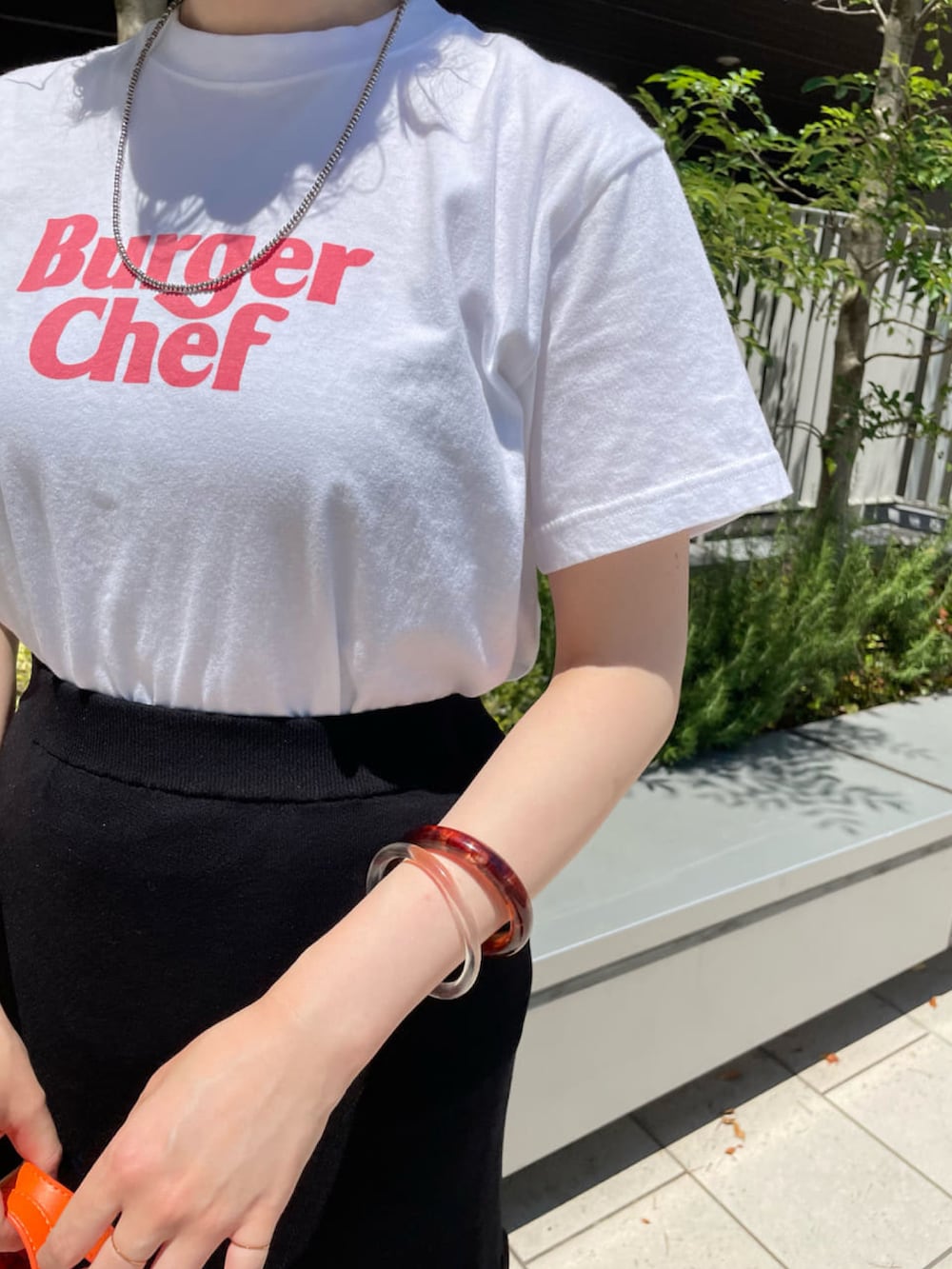 オレンジ系のトートバッグ、ブラック系のスカート、ホワイト系のTシャツ/カットソーを着用したレディースの夏コーディネートの3枚目の写真