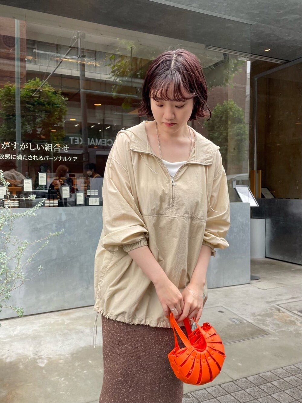 オレンジ系のトートバッグ、ブラウン系のスカート、ベージュ系のブルゾンを着用したレディースの夏コーディネートの5枚目の写真