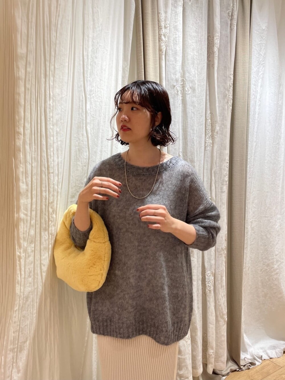 ブルー系のニット/セーター、オレンジ系のハンドバッグ、ホワイト系のスカートを着用したレディースの秋コーディネートの3枚目の写真