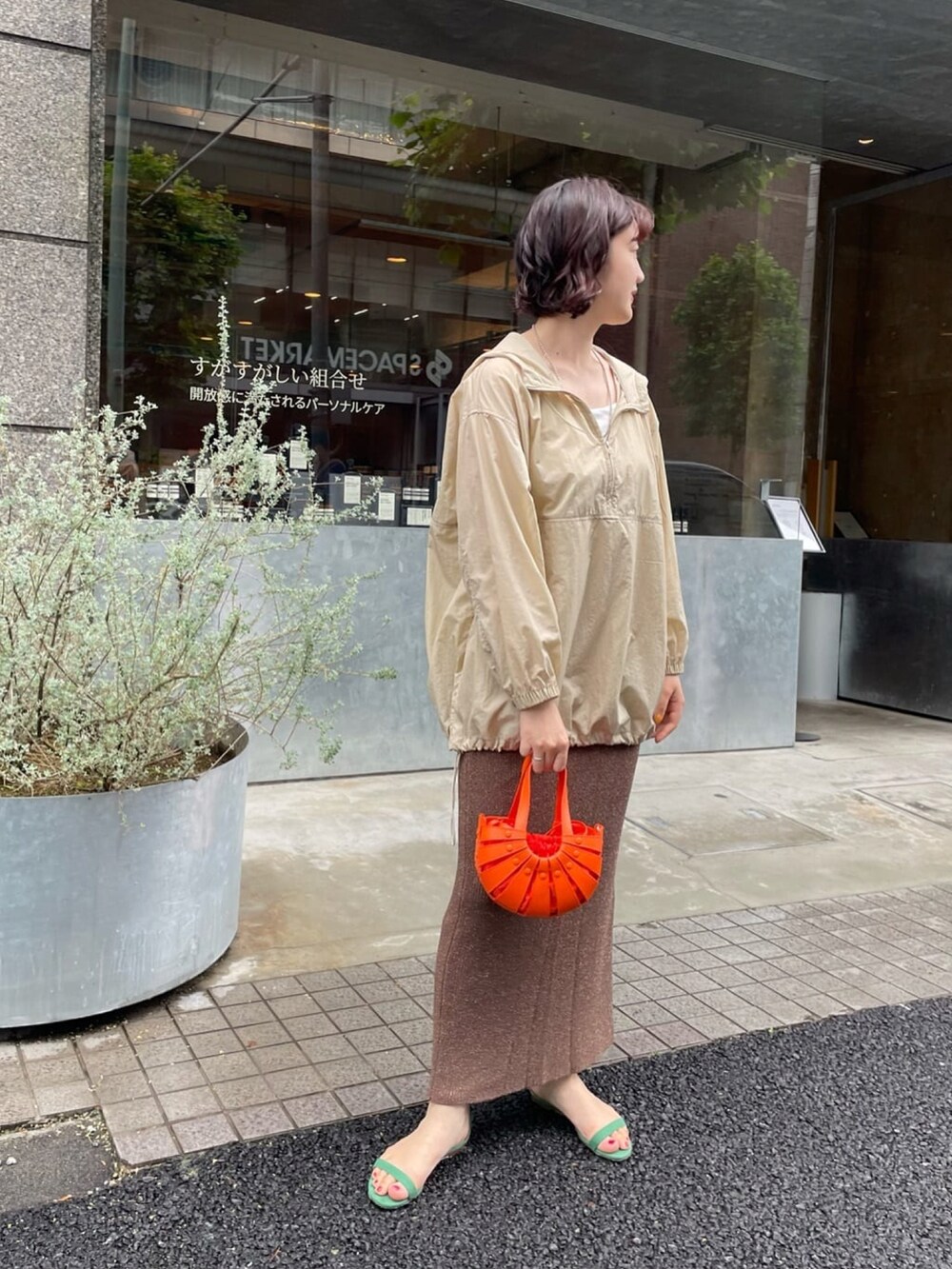 オレンジ系のトートバッグ、ブラウン系のスカート、ベージュ系のブルゾンを着用したレディースの夏コーディネートの3枚目の写真