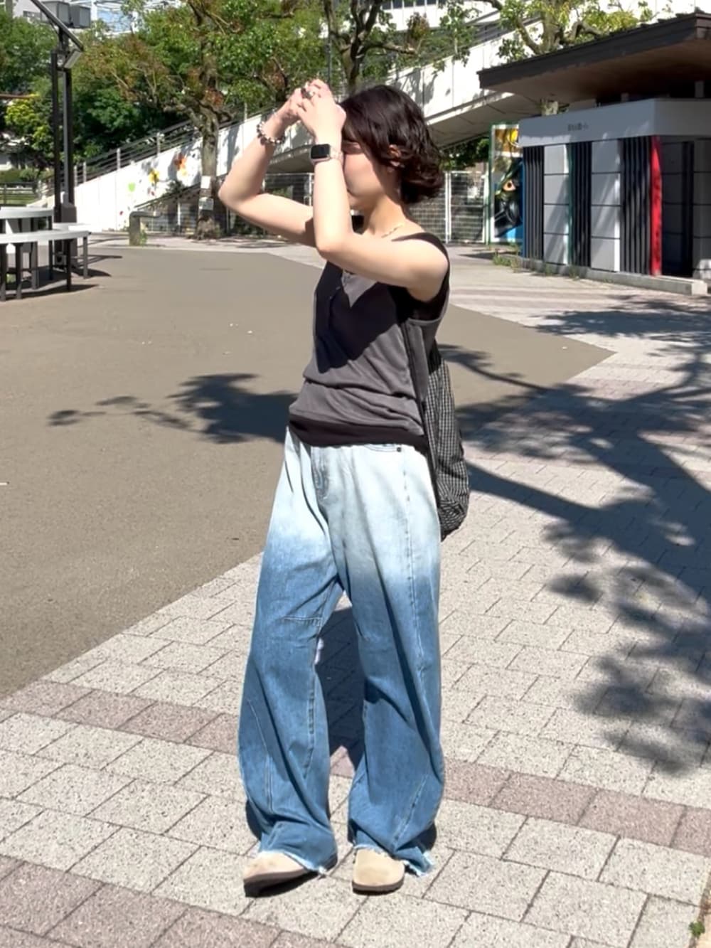 ブルー系のデニムパンツ、ベージュ系のサンダル、ブラック系のトップスを着用したレディースの夏コーディネートの3枚目の写真