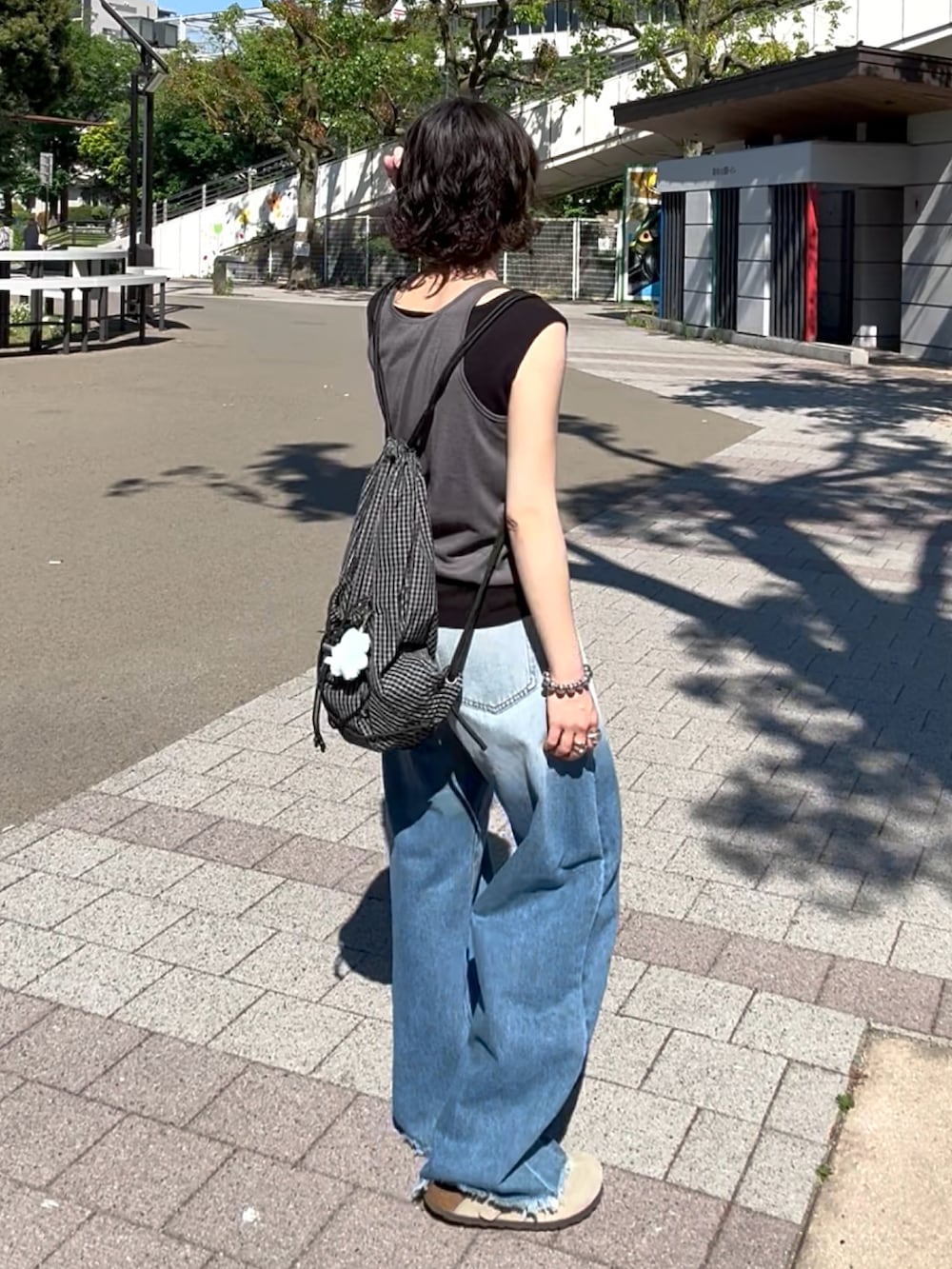 ブルー系のデニムパンツ、ベージュ系のサンダル、ブラック系のトップスを着用したレディースの夏コーディネートの4枚目の写真