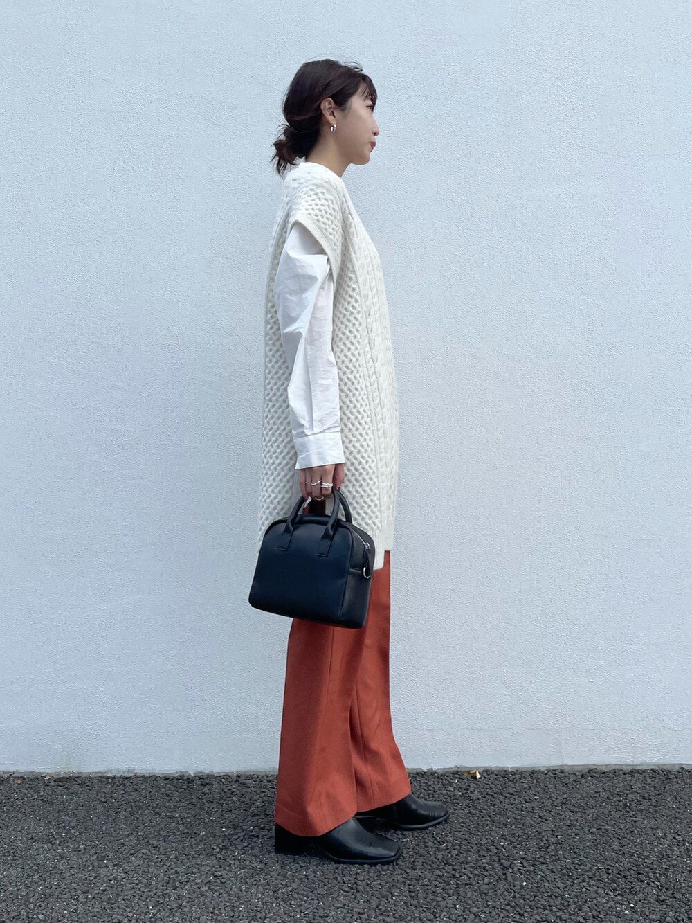 ホワイト系のベスト、オレンジ系のその他パンツ、ブラック系のボストンバッグを着用したレディースの秋コーディネートの2枚目の写真