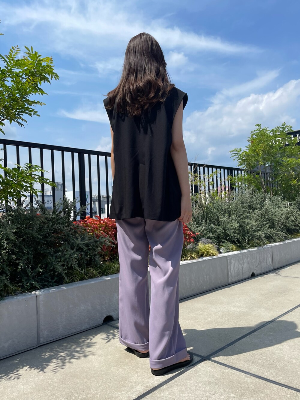 パープル系のスラックス、ブラック系のベスト、ブラック系のサンダルを着用したレディースの夏コーディネートの4枚目の写真