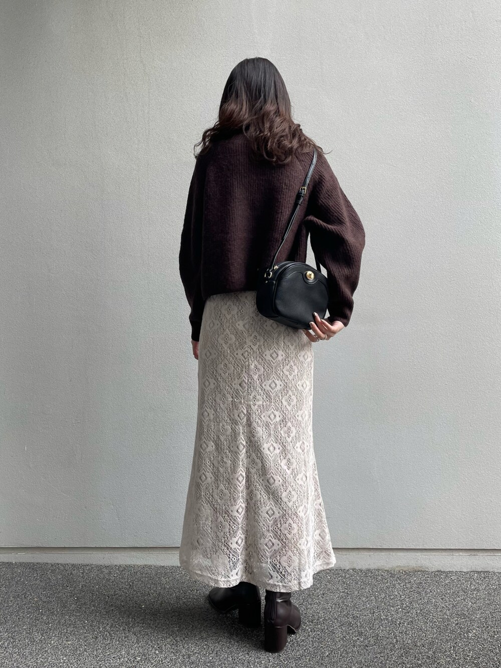 ブラウン系のニット/セーター、ホワイト系のスカート、ブラック系のショルダーバッグを着用したレディースの冬コーディネートの2枚目の写真
