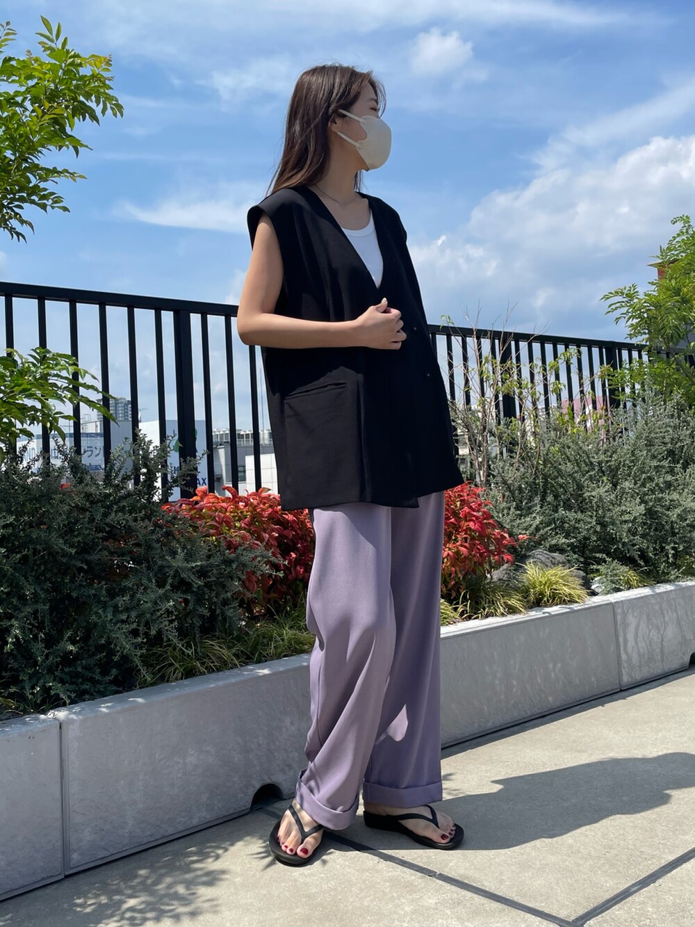 パープル系のスラックス、ブラック系のベスト、ブラック系のサンダルを着用したレディースの夏コーディネートの3枚目の写真