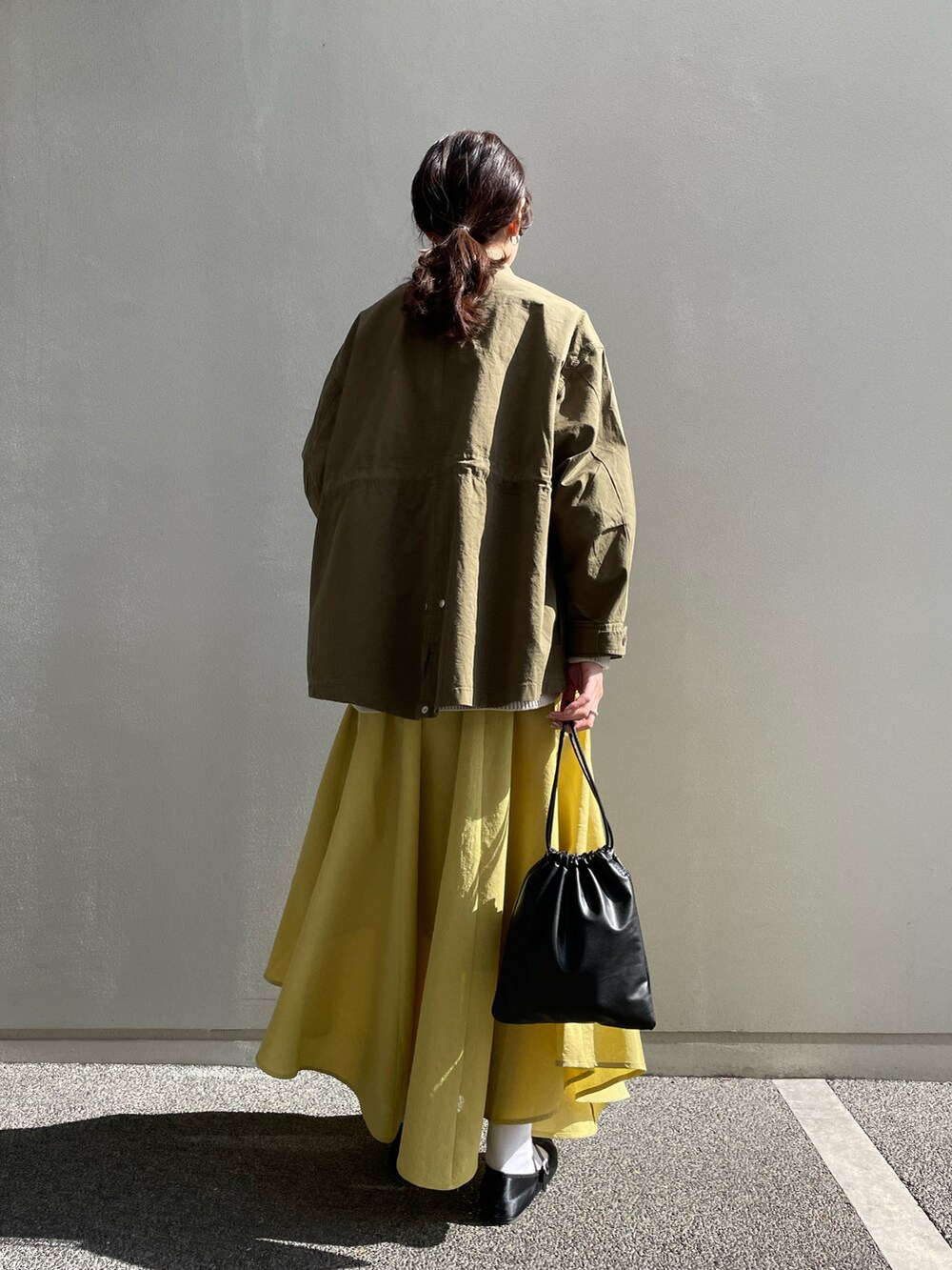 グリーン系のミリタリージャケット、ホワイト系のニット/セーター、イエロー系のスカートを着用したレディースの冬コーディネートの3枚目の写真