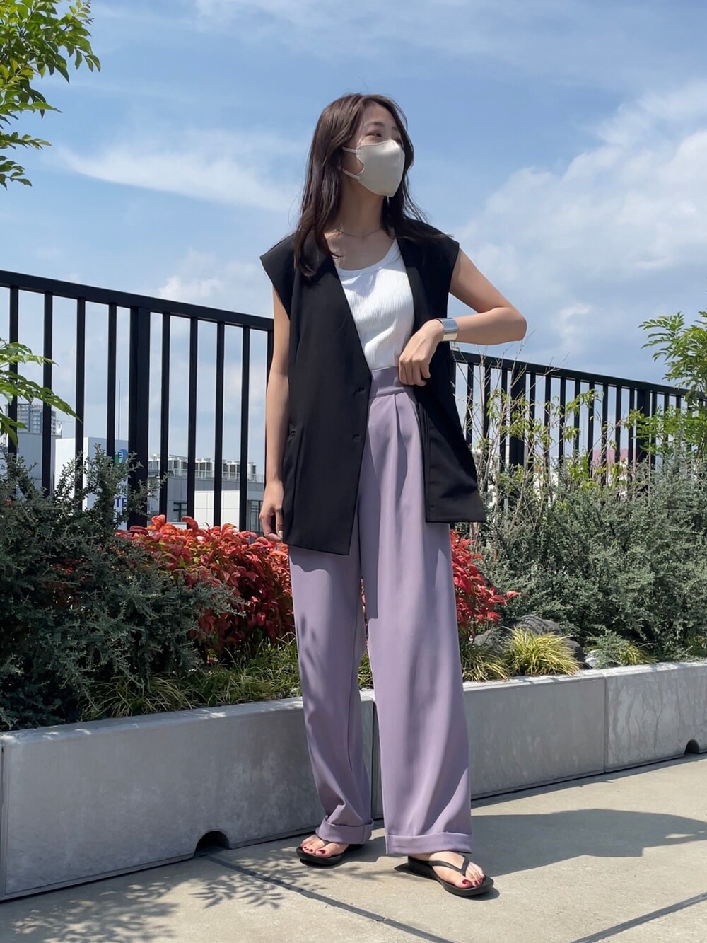 パープル系のスラックス、ブラック系のベスト、ブラック系のサンダルを着用したレディースの夏コーディネートの2枚目の写真