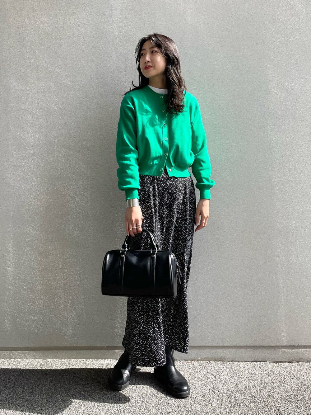 グリーン系のカーディガン/ボレロ、ブラック系のボストンバッグ、ブラック系のスカートを着用したレディースの春コーディネートの2枚目の写真