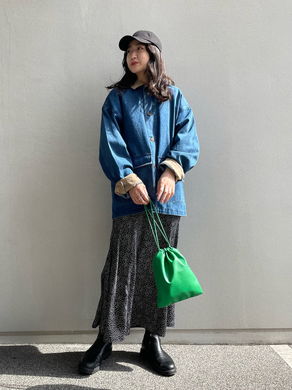 ブルー系のカバーオール、ブラック系のスカート、グリーン系のショルダーバッグを着用したレディースの春コーディネートの3枚目の写真
