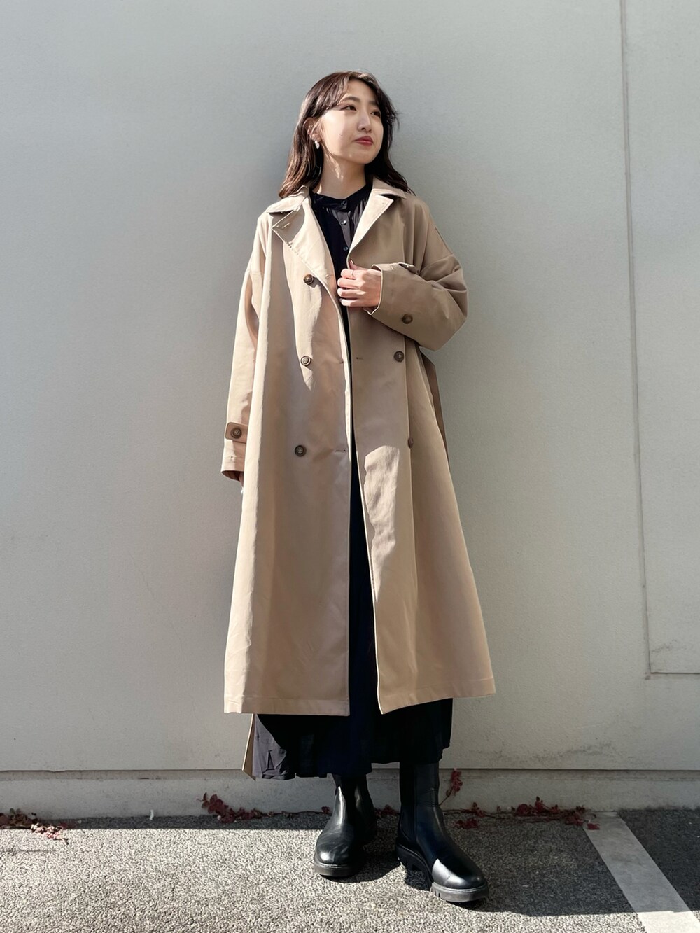 ベージュ系のステンカラーコート、ブラック系のワンピースを着用したレディースの冬コーディネートの2枚目の写真