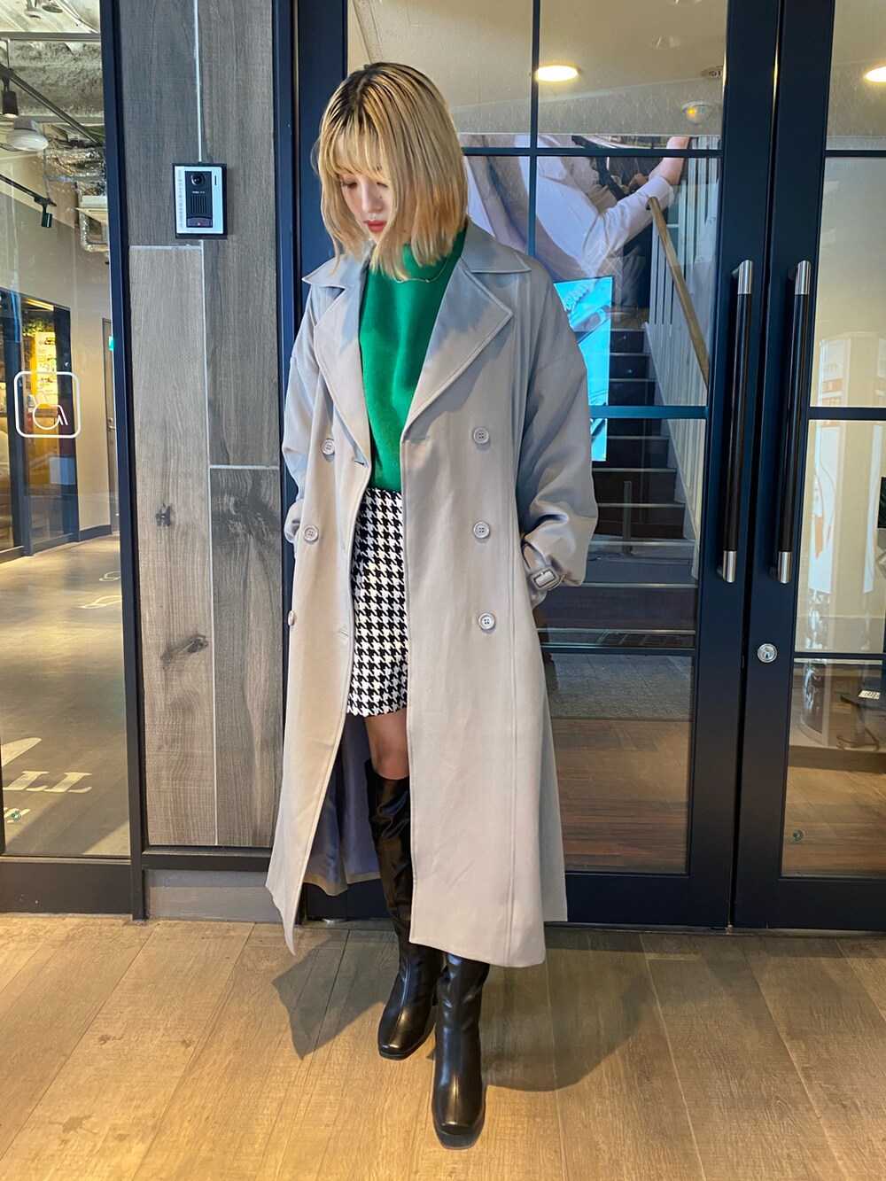 グリーン系のニット/セーター、ベージュ系のトレンチコート、ホワイト系のパンツを着用したレディースの秋コーディネートの2枚目の写真