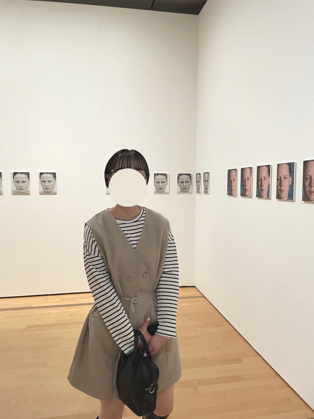 ブラック系のハンドバッグ、ベージュ系のベスト、ブラック系のブーツを着用したレディースの春コーディネートの2枚目の写真