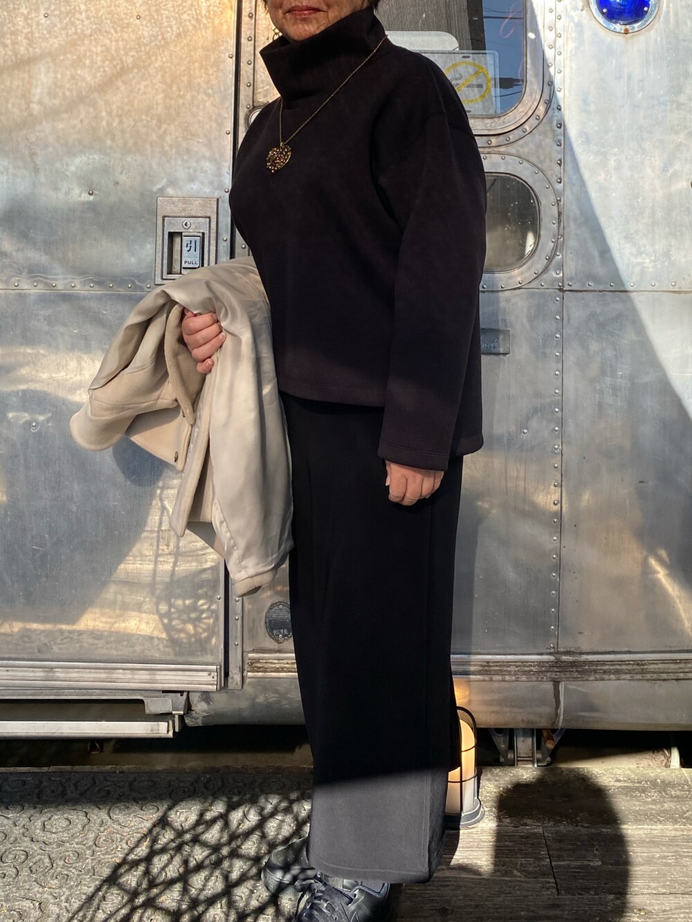 ベージュ系のステンカラーコート、ブラック系のTシャツ/カットソー、レッド系のバッグを着用したレディースの冬コーディネートの2枚目の写真