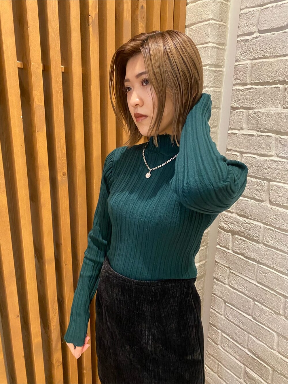 ブラック系のスカート、ホワイト系のダウンジャケット/コート、グリーン系のニット/セーターを着用したレディースの冬コーディネートの2枚目の写真