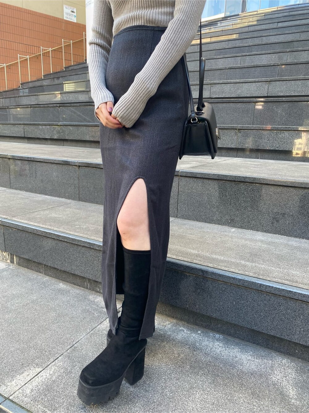 グレー系のニット/セーター、ブラック系のブーツ、ブラック系のスカートを着用したレディースの冬コーディネートの6枚目の写真