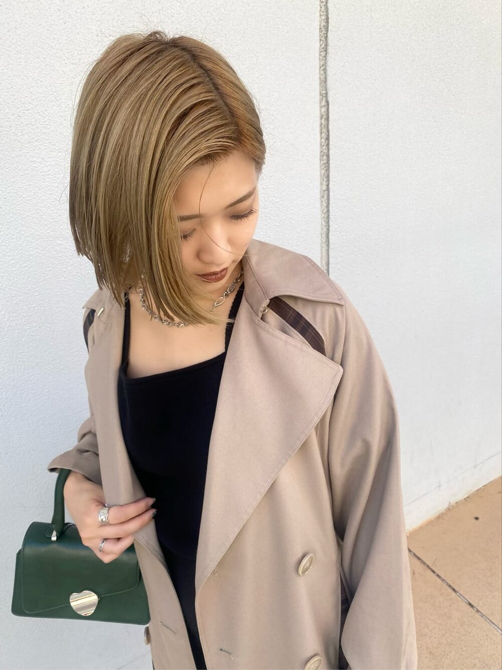 ベージュ系のトレンチコート、ブラック系のスカート、グリーン系のハンドバッグを着用したレディースの夏コーディネートの3枚目の写真
