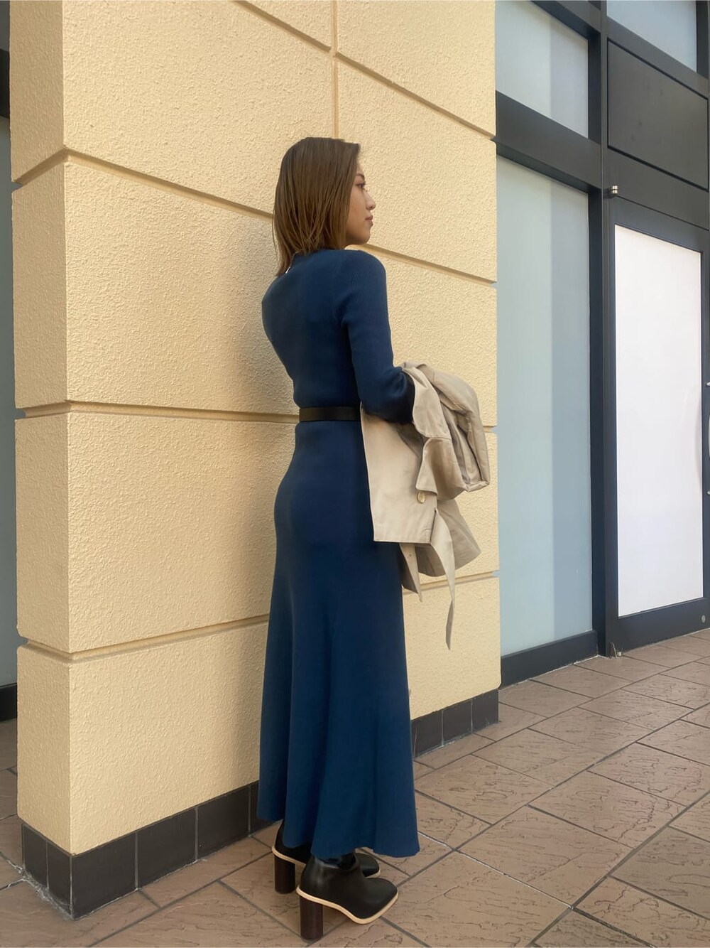 ブルー系のワンピース、ベージュ系のトレンチコート、ブラック系のブーツを着用したレディースの冬コーディネートの2枚目の写真