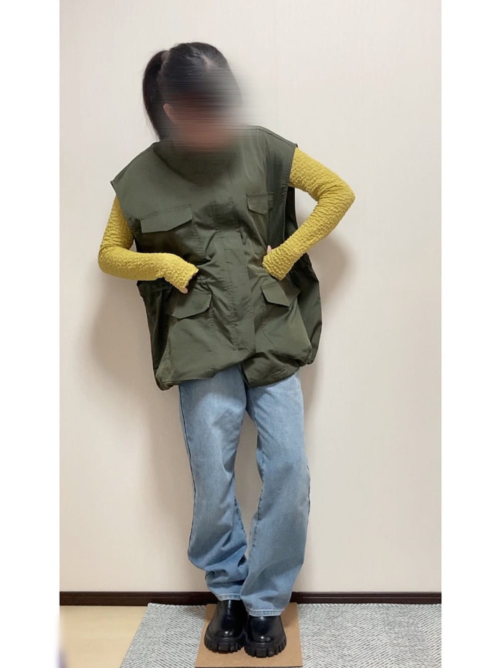 ブルー系のデニムパンツ、ブラック系のブーツ、グリーン系のベストを着用したレディースの春コーディネートの3枚目の写真