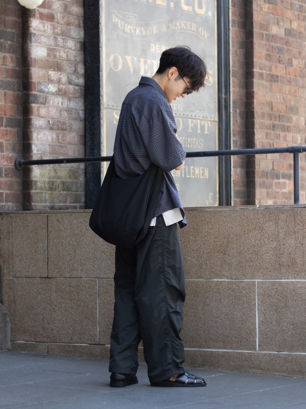 ブラック系のショルダーバッグ、ブラック系のサンダル、グレー系のパンツを着用したメンズの夏コーディネートの5枚目の写真