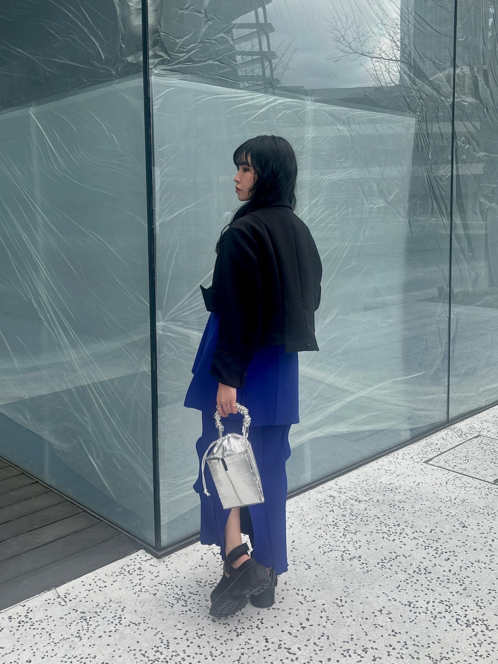 ブラック系のテーラードジャケット、ブルー系のニット/セーター、ブルー系のスカートを着用したレディースの春コーディネートの5枚目の写真