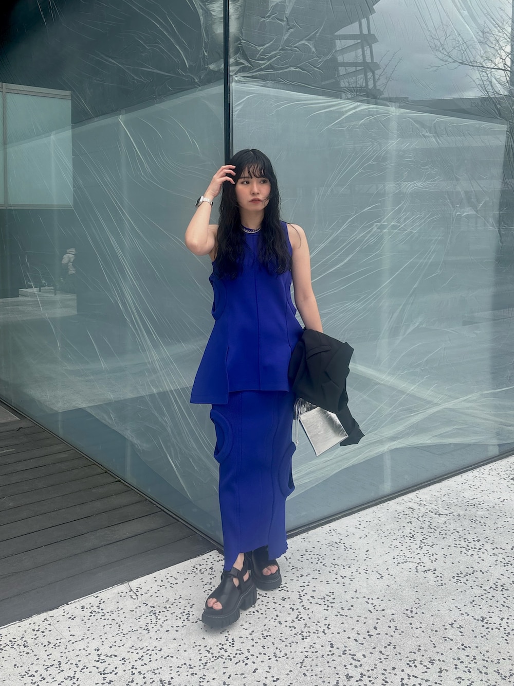 ブラック系のテーラードジャケット、ブルー系のニット/セーター、ブルー系のスカートを着用したレディースの春コーディネートの3枚目の写真