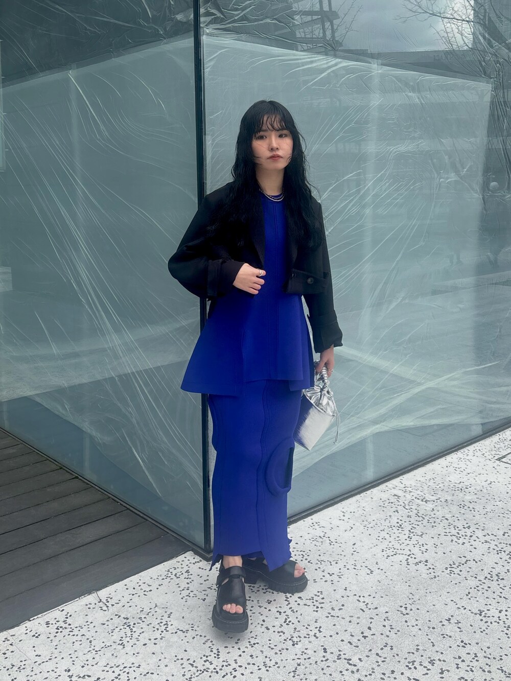 ブラック系のテーラードジャケット、ブルー系のニット/セーター、ブルー系のスカートを着用したレディースの春コーディネートの2枚目の写真