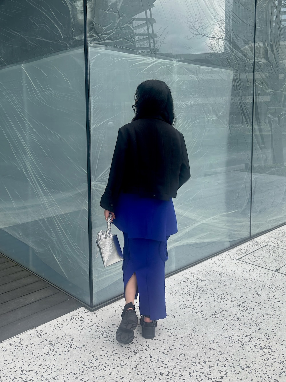 ブラック系のテーラードジャケット、ブルー系のニット/セーター、ブルー系のスカートを着用したレディースの春コーディネートの4枚目の写真