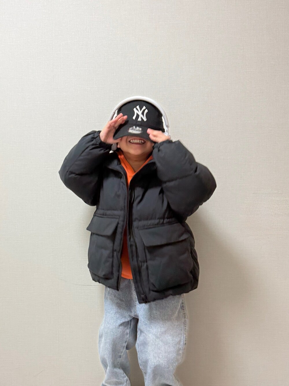 ブラック系のジャケット/アウター、ブラック系のスニーカー、オレンジ系のパーカーを着用したキッズの冬コーディネートの2枚目の写真