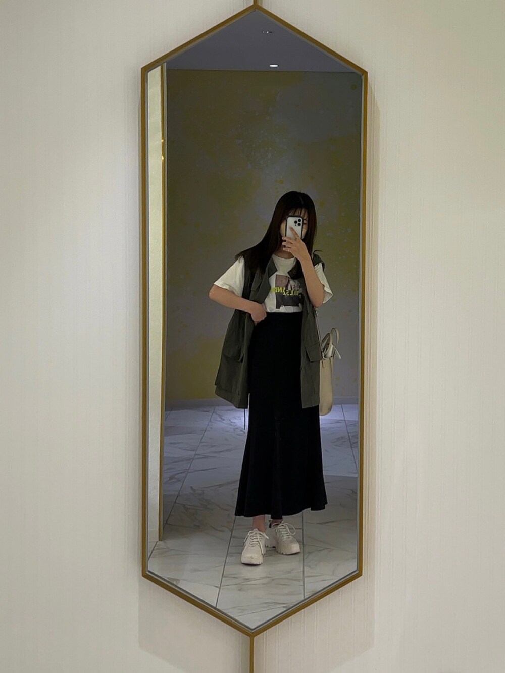 グリーン系のベスト、ブラック系のスカートを着用したレディースの秋コーディネートの2枚目の写真