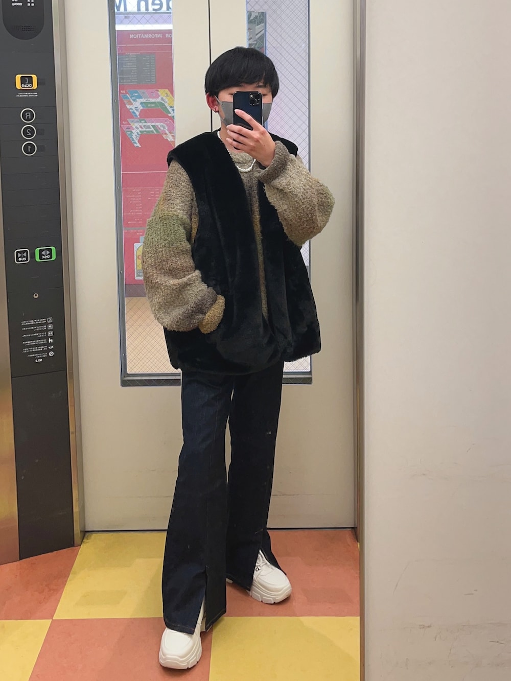 ブラック系のベスト、ブルー系のデニムパンツ、ホワイト系のスニーカーを着用したメンズの冬コーディネートの2枚目の写真