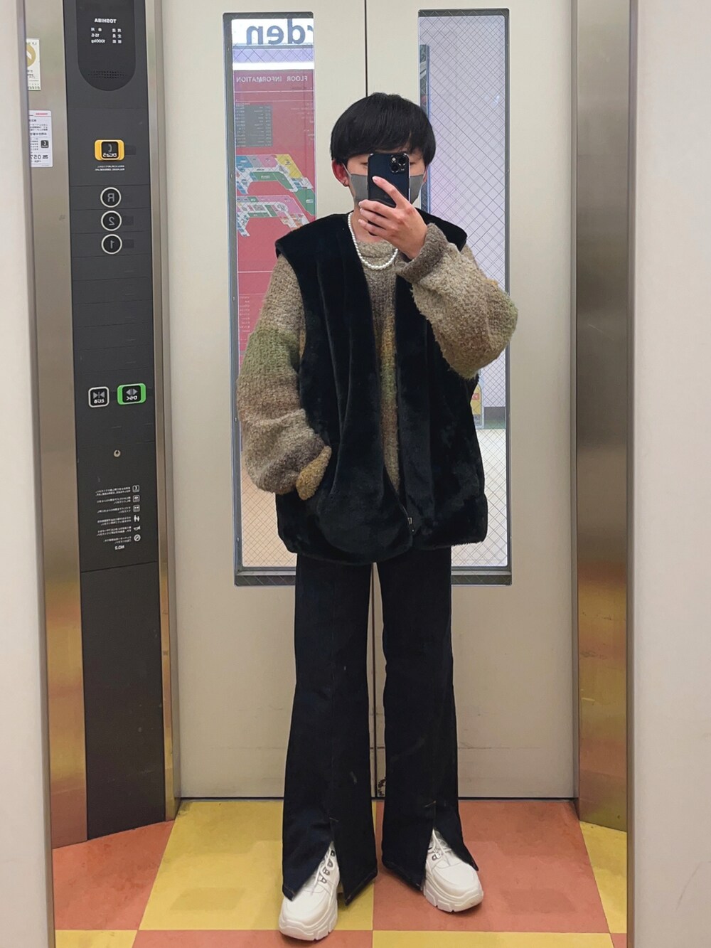 ブラック系のベスト、ブルー系のデニムパンツ、ホワイト系のスニーカーを着用したメンズの冬コーディネートの3枚目の写真