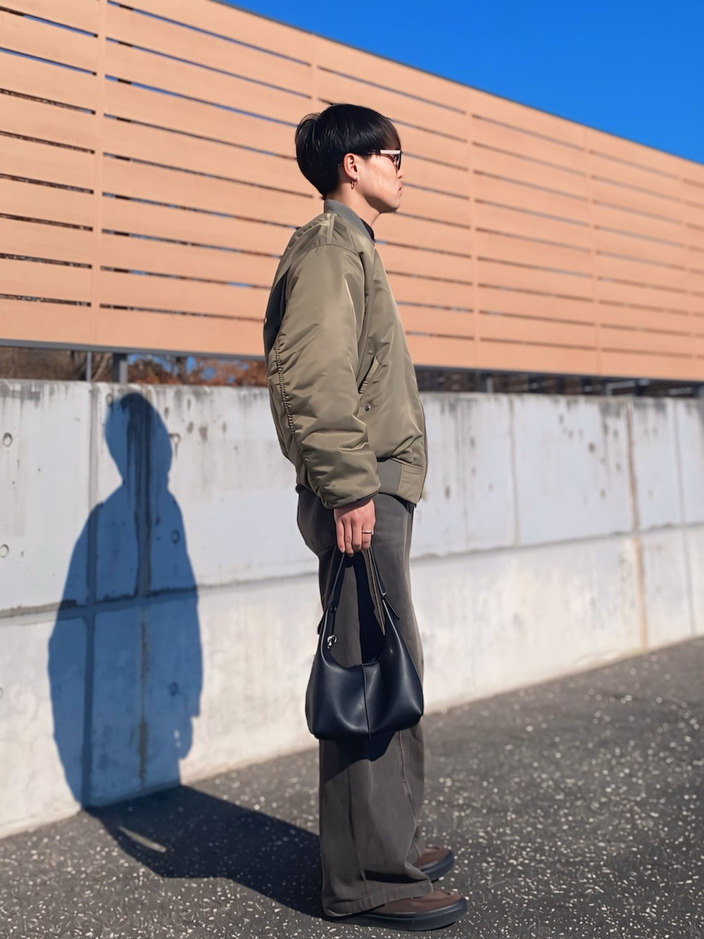 ブラック系のデニムパンツ、ブラック系のハンドバッグ、ブラウン系のスニーカーを着用したメンズの冬コーディネートの2枚目の写真