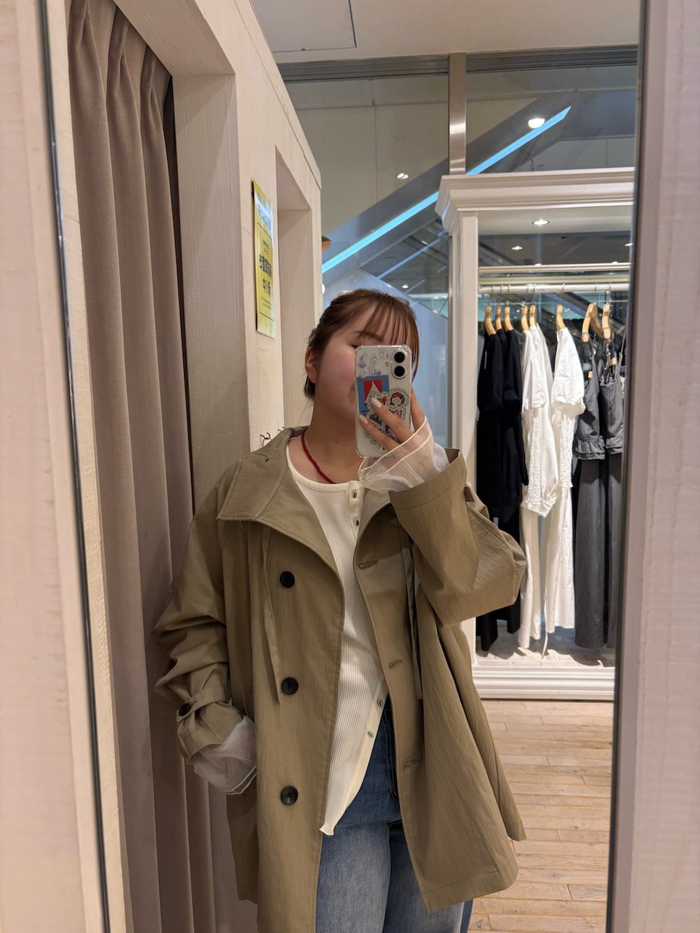 ベージュ系のトレンチコート、ホワイト系のカーディガン/ボレロ、ブルー系のデニムパンツを着用したレディースの春コーディネートの2枚目の写真