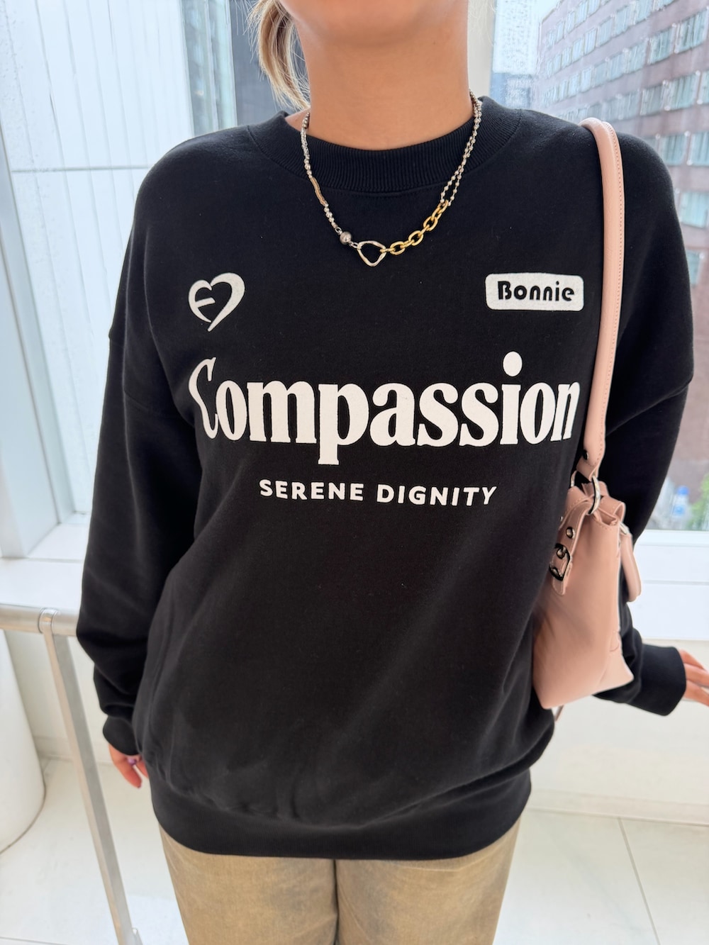 ブラック系のスウェット、ピンク系のショルダーバッグ、ブラウン系のデニムパンツを着用したレディースの秋コーディネートの5枚目の写真
