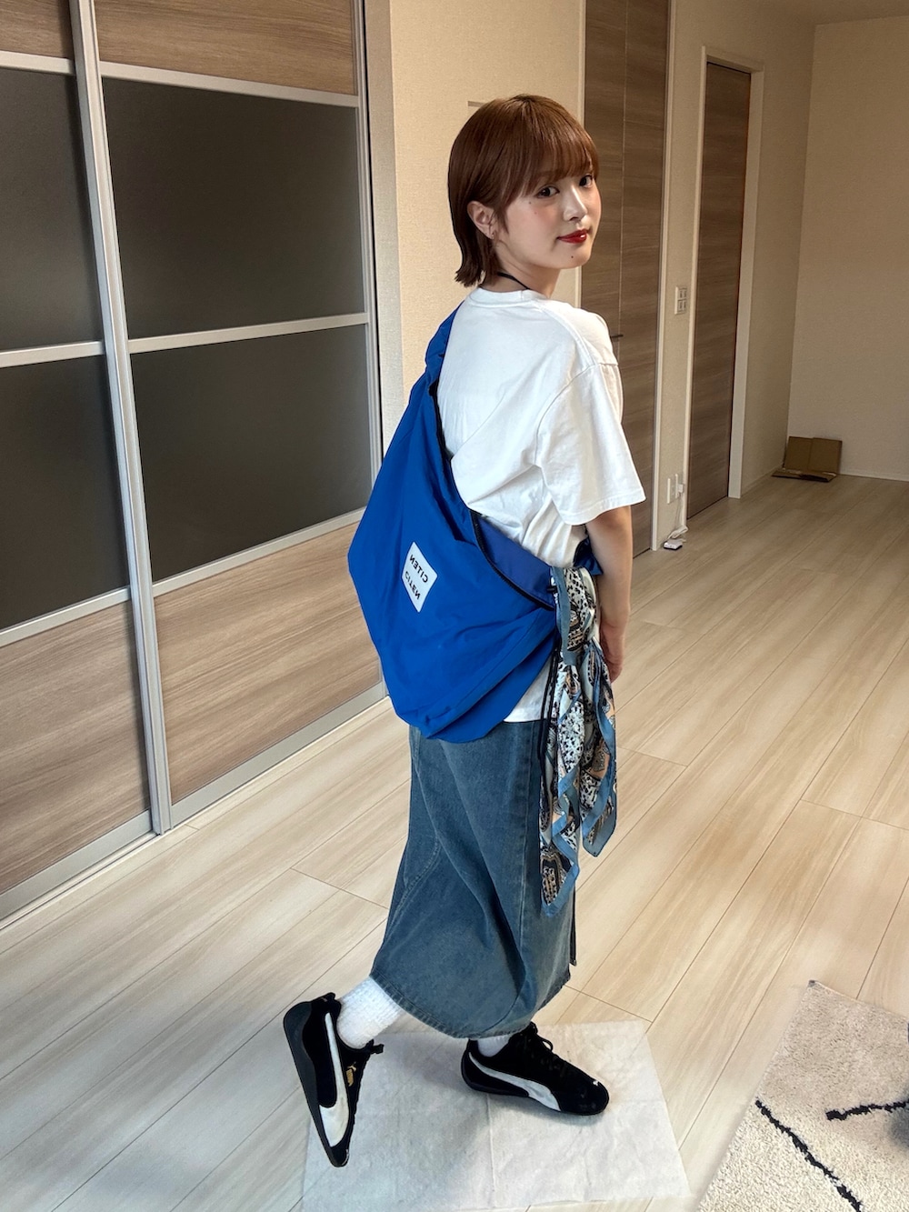 ブルー系のデニムスカート、ホワイト系のTシャツ/カットソー、ブルー系のショルダーバッグを着用したレディースの夏コーディネートの2枚目の写真